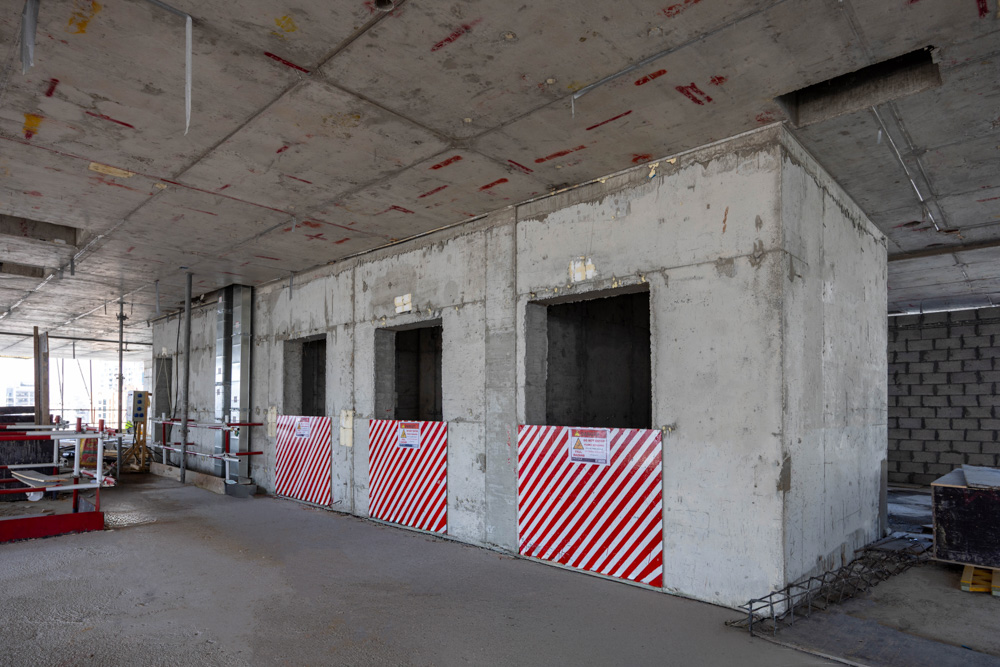 Cove Edition I By Imtiaz 1 Interior of a building under construction featuring concrete walls and striped hazard barriers.
